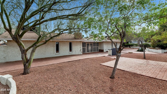 exterior space with stucco siding, roof with shingles, and a patio