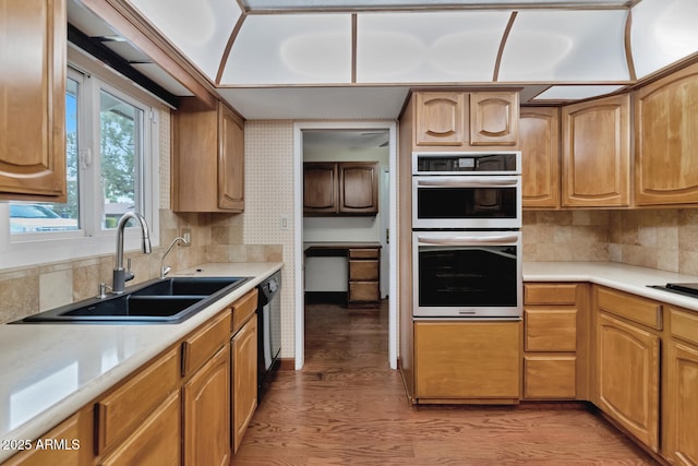 kitchen with double oven, black dishwasher, light countertops, and a sink