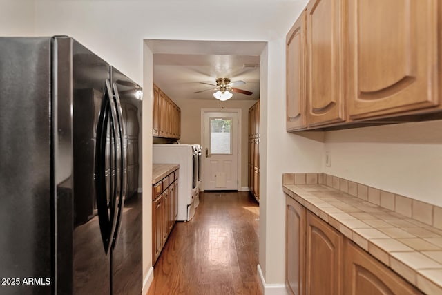 kitchen with a ceiling fan, tile countertops, washer / clothes dryer, wood finished floors, and freestanding refrigerator