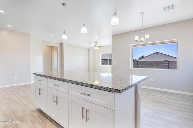 kitchen featuring stone counters, white cabinetry, a center island, decorative light fixtures, and ceiling fan with notable chandelier