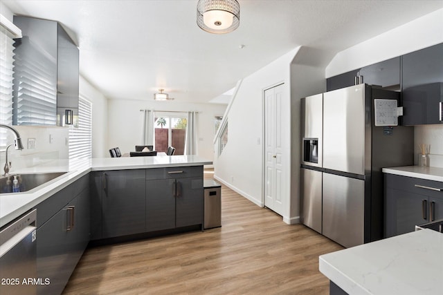 kitchen featuring gray cabinets, appliances with stainless steel finishes, sink, kitchen peninsula, and light wood-type flooring