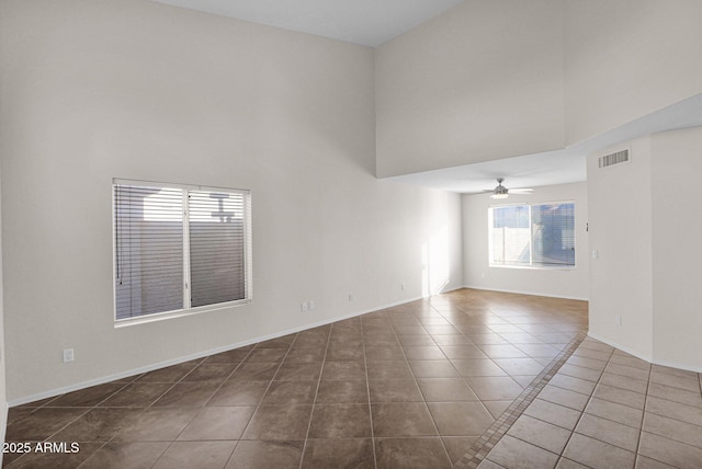 spare room featuring ceiling fan, a high ceiling, and dark tile patterned floors