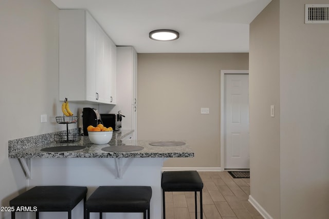 kitchen featuring visible vents, baseboards, a breakfast bar, a peninsula, and white cabinetry