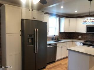 kitchen with white cabinetry, hanging light fixtures, black appliances, and sink