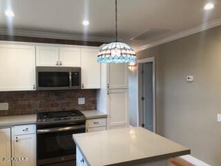 kitchen with hanging light fixtures, crown molding, white cabinetry, appliances with stainless steel finishes, and tasteful backsplash