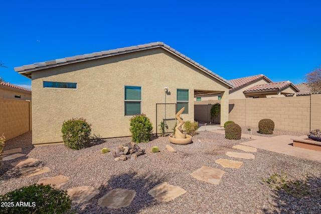 rear view of house with stucco siding, a tile roof, a fenced backyard, and a patio area