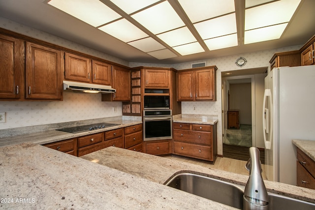 kitchen with stainless steel appliances, wood-type flooring, sink, and light stone countertops