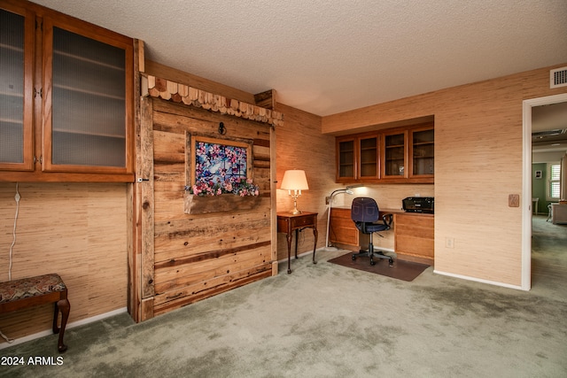 carpeted office with a textured ceiling, wooden walls, and built in desk