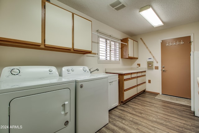 laundry area with light wood-type flooring, a textured ceiling, cabinets, sink, and washer and dryer