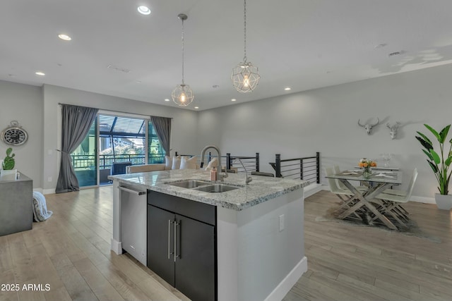 kitchen featuring dishwasher, sink, hanging light fixtures, a kitchen island with sink, and light wood-type flooring