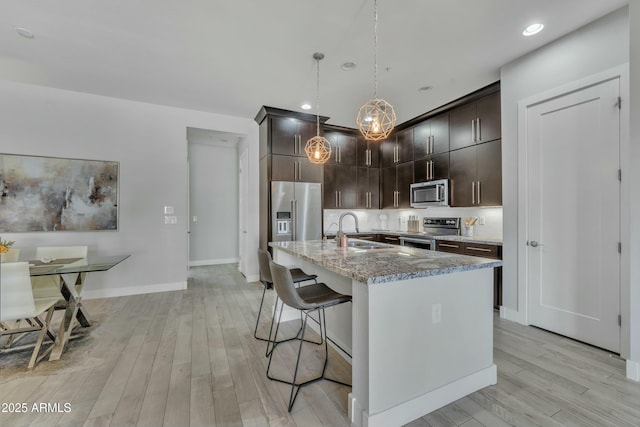 kitchen featuring pendant lighting, sink, light hardwood / wood-style flooring, dark brown cabinetry, and stainless steel appliances