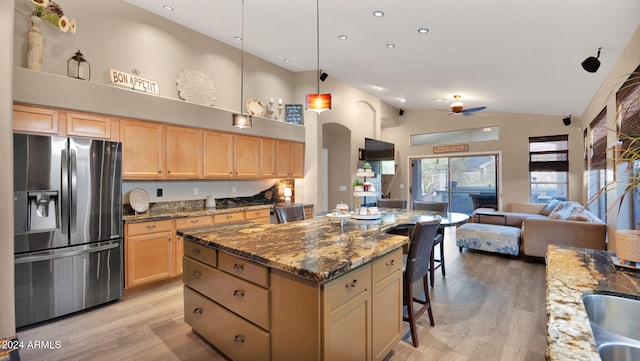 kitchen featuring stainless steel fridge with ice dispenser, high vaulted ceiling, dark stone counters, and a kitchen island