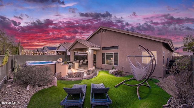 back house at dusk with a yard and a hot tub