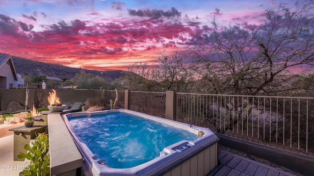 pool at dusk with a mountain view, a hot tub, and an outdoor fire pit