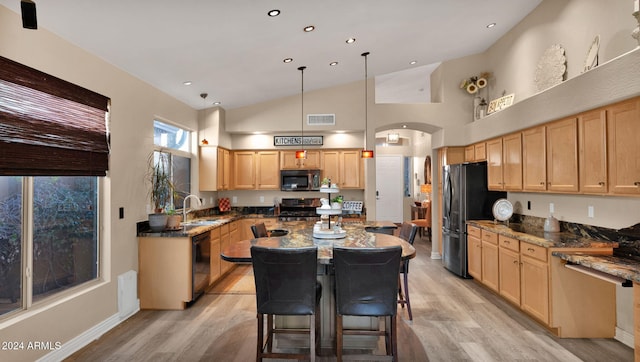 kitchen with a kitchen breakfast bar, dark stone counters, black appliances, pendant lighting, and light hardwood / wood-style floors