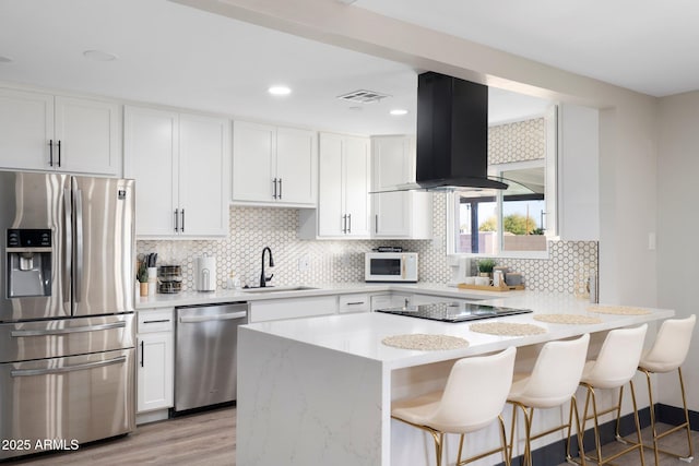 kitchen with stainless steel appliances, island exhaust hood, a sink, light countertops, and a breakfast bar area