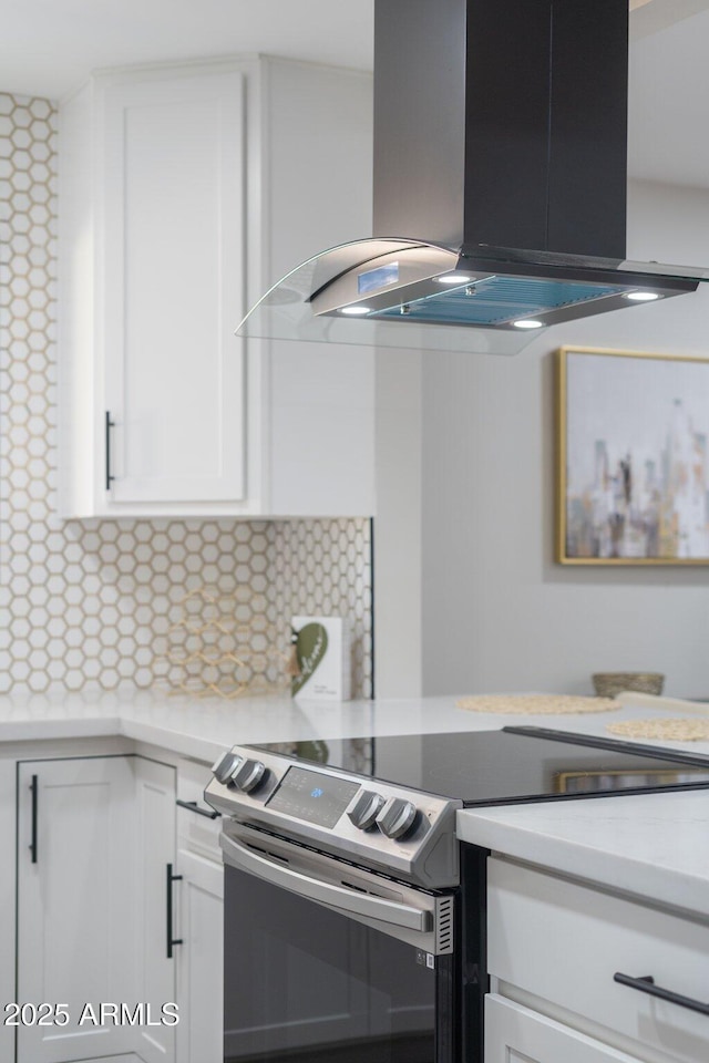kitchen featuring island exhaust hood, stainless steel range with electric stovetop, white cabinetry, decorative backsplash, and light countertops
