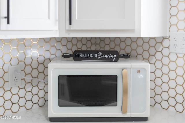 kitchen view of white microwave, white cabinetry, and light countertops