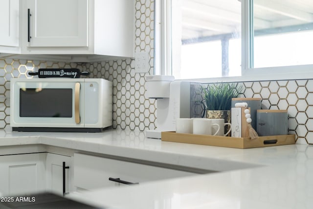 kitchen view of white microwave, tasteful backsplash, white cabinetry, and light countertops