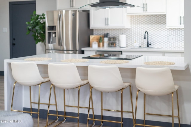 kitchen featuring stainless steel fridge with ice dispenser, a sink, white cabinets, light countertops, and decorative backsplash