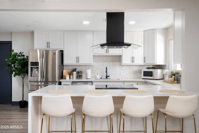 kitchen featuring stainless steel appliances, island exhaust hood, a sink, light countertops, and a breakfast bar area