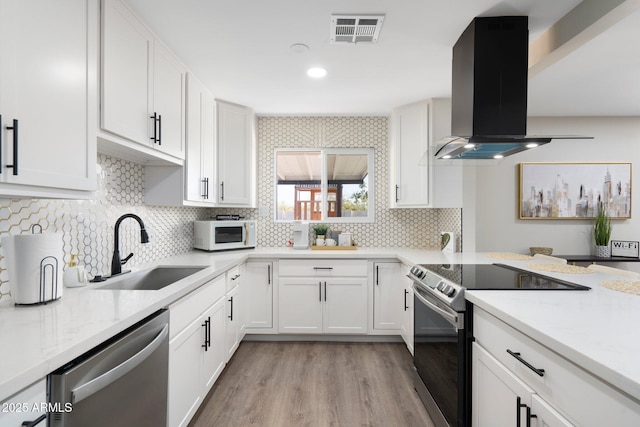 kitchen featuring appliances with stainless steel finishes, island range hood, a sink, light wood-style flooring, and white cabinets