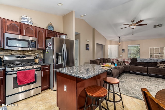 kitchen featuring ceiling fan, light tile patterned floors, stainless steel appliances, a breakfast bar area, and vaulted ceiling