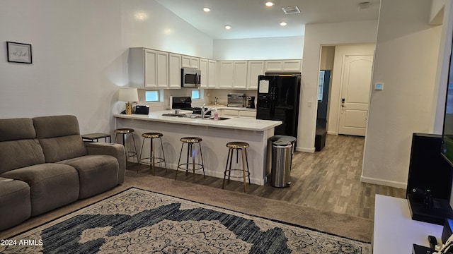 kitchen with black refrigerator with ice dispenser, kitchen peninsula, white cabinets, and a kitchen bar