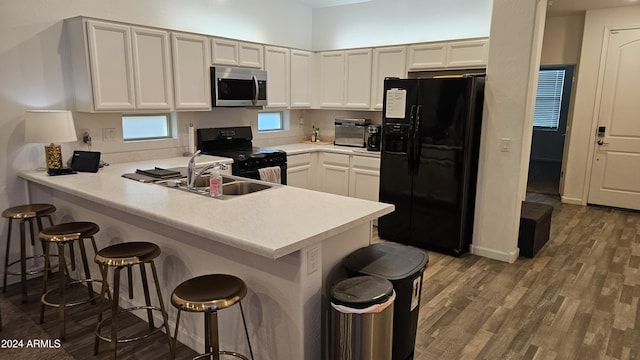 kitchen with sink, a kitchen breakfast bar, kitchen peninsula, hardwood / wood-style floors, and black appliances