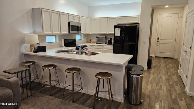 kitchen with a breakfast bar area, white cabinetry, black appliances, dark hardwood / wood-style flooring, and kitchen peninsula