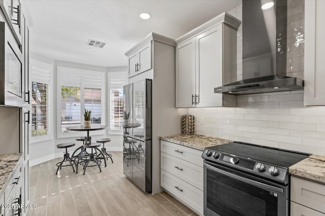 kitchen featuring stainless steel range with electric cooktop, refrigerator, wall chimney range hood, light stone countertops, and backsplash