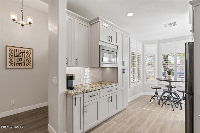 kitchen with built in microwave, light wood-type flooring, tasteful backsplash, and white cabinets