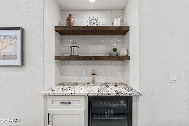 bar with backsplash, beverage cooler, light stone countertops, and white cabinets