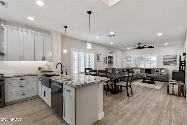 kitchen with white cabinetry, sink, light stone counters, and hanging light fixtures