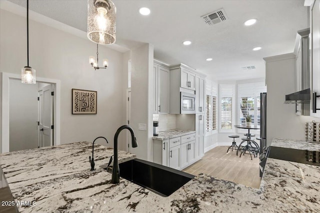 kitchen with sink, stainless steel appliances, white cabinets, decorative light fixtures, and light wood-type flooring