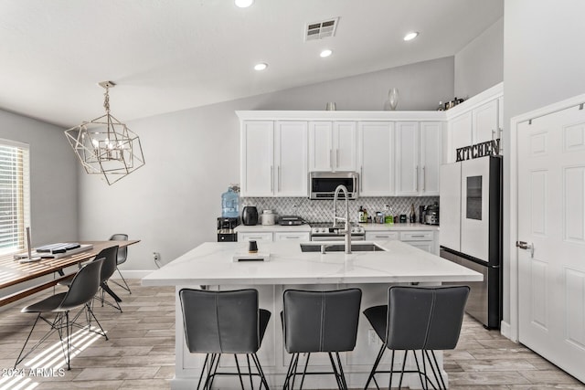 kitchen with a center island with sink, refrigerator, white cabinetry, and vaulted ceiling