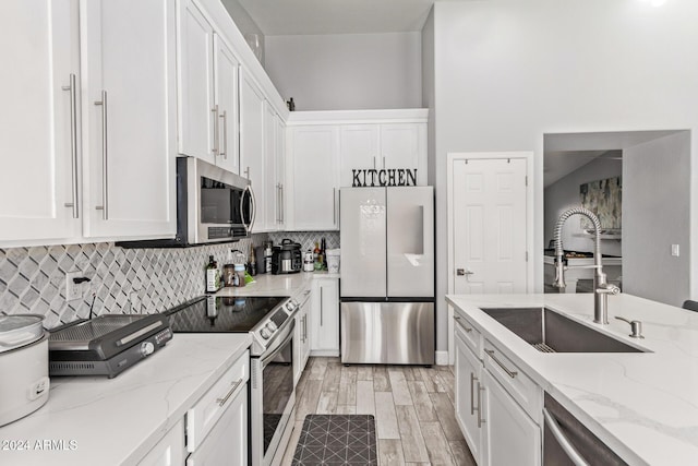 kitchen featuring light stone countertops, appliances with stainless steel finishes, light wood-type flooring, sink, and white cabinets