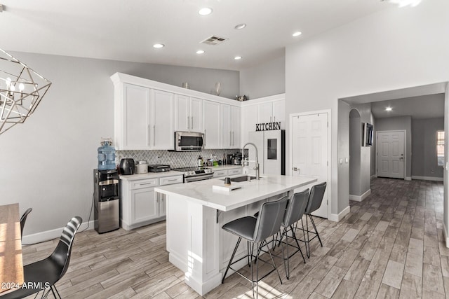 kitchen featuring white cabinets, sink, light wood-type flooring, a kitchen bar, and stainless steel appliances