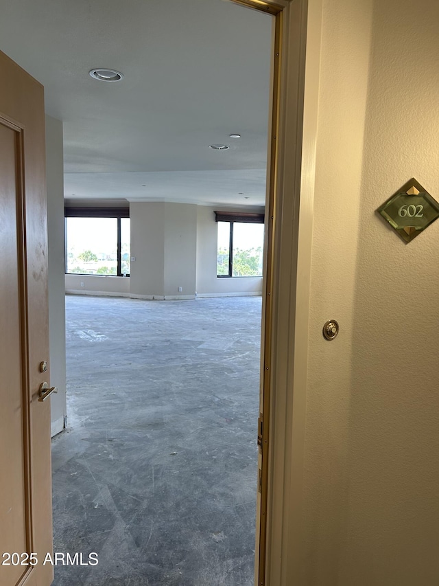 corridor with recessed lighting, baseboards, plenty of natural light, and unfinished concrete floors
