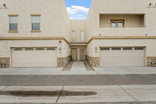 townhome / multi-family property featuring stone siding, stucco siding, an attached garage, and a balcony