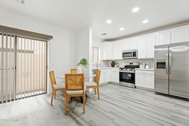 kitchen with light countertops, white cabinets, appliances with stainless steel finishes, light wood-type flooring, and backsplash