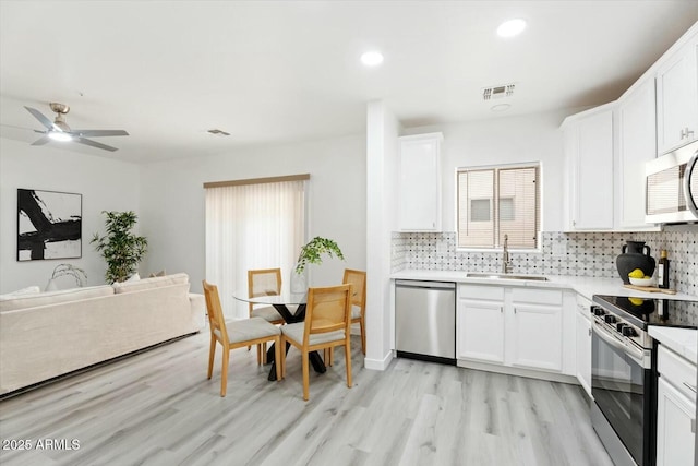 kitchen featuring visible vents, a sink, decorative backsplash, stainless steel appliances, and white cabinets