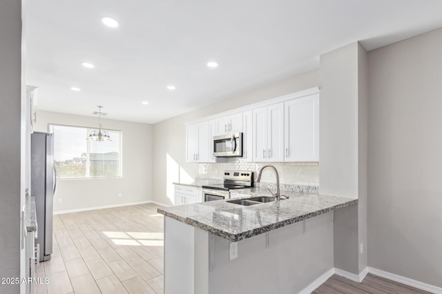 kitchen with a kitchen breakfast bar, hanging light fixtures, appliances with stainless steel finishes, sink, and white cabinets