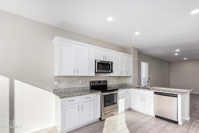 kitchen featuring white cabinets, appliances with stainless steel finishes, sink, kitchen peninsula, and light stone counters