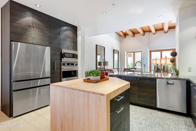 kitchen with wooden counters, stainless steel appliances, sink, vaulted ceiling with beams, and a kitchen island