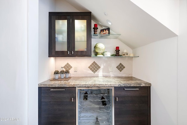 bar with tasteful backsplash, dark brown cabinetry, beverage cooler, and lofted ceiling