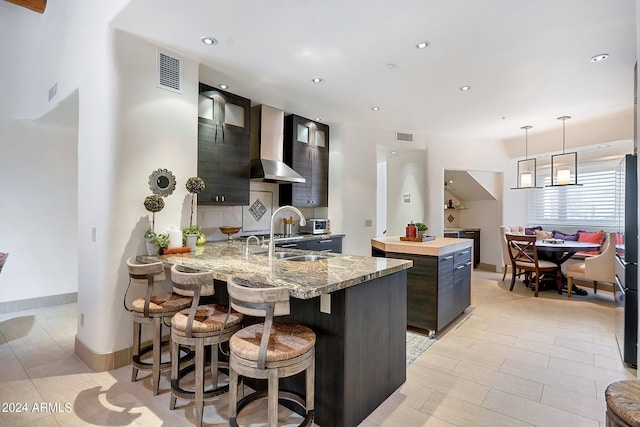 kitchen featuring kitchen peninsula, sink, wall chimney range hood, pendant lighting, and a kitchen island