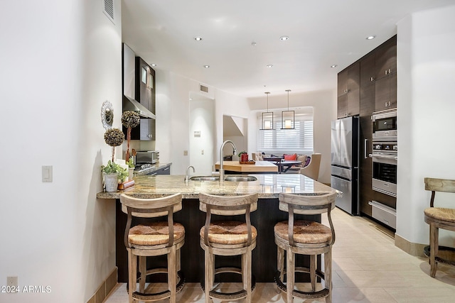 kitchen with a breakfast bar area, dark brown cabinets, stainless steel appliances, and sink