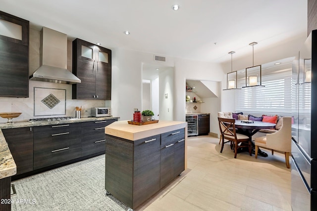 kitchen featuring wall chimney exhaust hood, dark brown cabinetry, stainless steel gas cooktop, decorative light fixtures, and a kitchen island