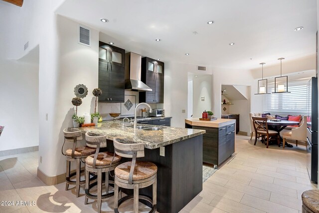 kitchen with dark brown cabinetry, lofted ceiling with beams, a kitchen island, and wall chimney exhaust hood